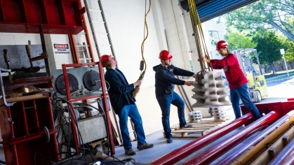 Two male students and one female student wearing hard hats while lifting concrete with an indoor crane.