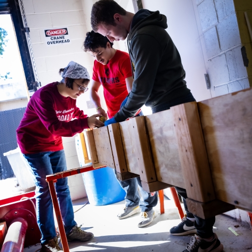 Three university students working in a construction lab on a wooden structure. One woman and two men. 