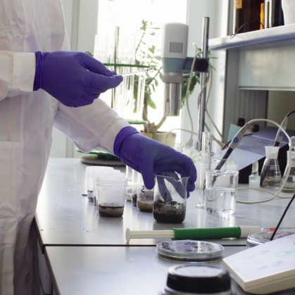 Hands of the scientist in laboratory mixing samples of the soil with water in the chemical beakers.