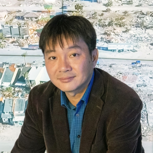 head shot of Asian male with sort black hair wearing a brown suit jacket and blue patterned shirt