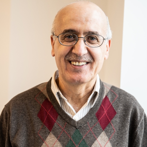 head shot of bald man in eyeglasses wearing a plaid pullover sweater