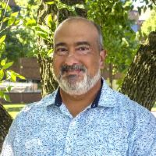 head shot of bald male with a grey beard wearing a blue and white patterned button down shirt