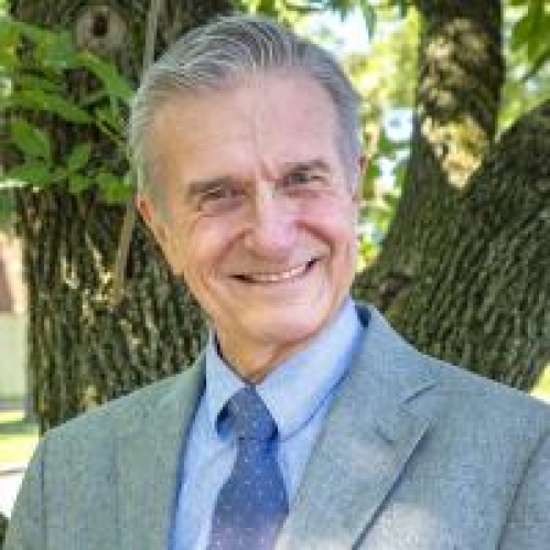 head shot of man with short grey hair wearing a light blue suit, light blue shirt, and blue patterned tie
