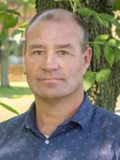 head shot of man wearing a dark blue patterned shirt
