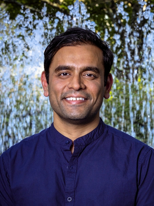 Headshot of male with short black hair wearing a dark blue button down shirt.