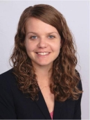head shot of female with curly long brown hair wearing a black suit jacket 
