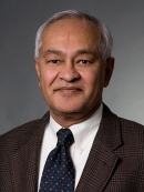 headshot of male with grey hair wearing a brown suit, patterned tie, and white shirt