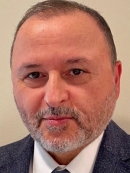 head shot of man with beard, short brown hair, wearing a dark blue suit, white shirt, and tie