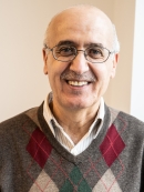 head shot of bald man in eyeglasses wearing a plaid pullover sweater
