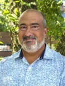 head shot of bald male with a grey beard wearing a blue and white patterned button down shirt