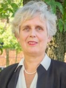 head shot of woman with short grey hair wearing a dark grey suit, white blouse, and pearl necklace.