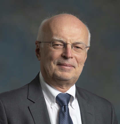 headshot of male with eyeglasses wearing a grey suit, blue tie and white shirt