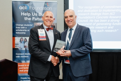 Male professor receives award from another male standing in front of an ACI Foundation banner.